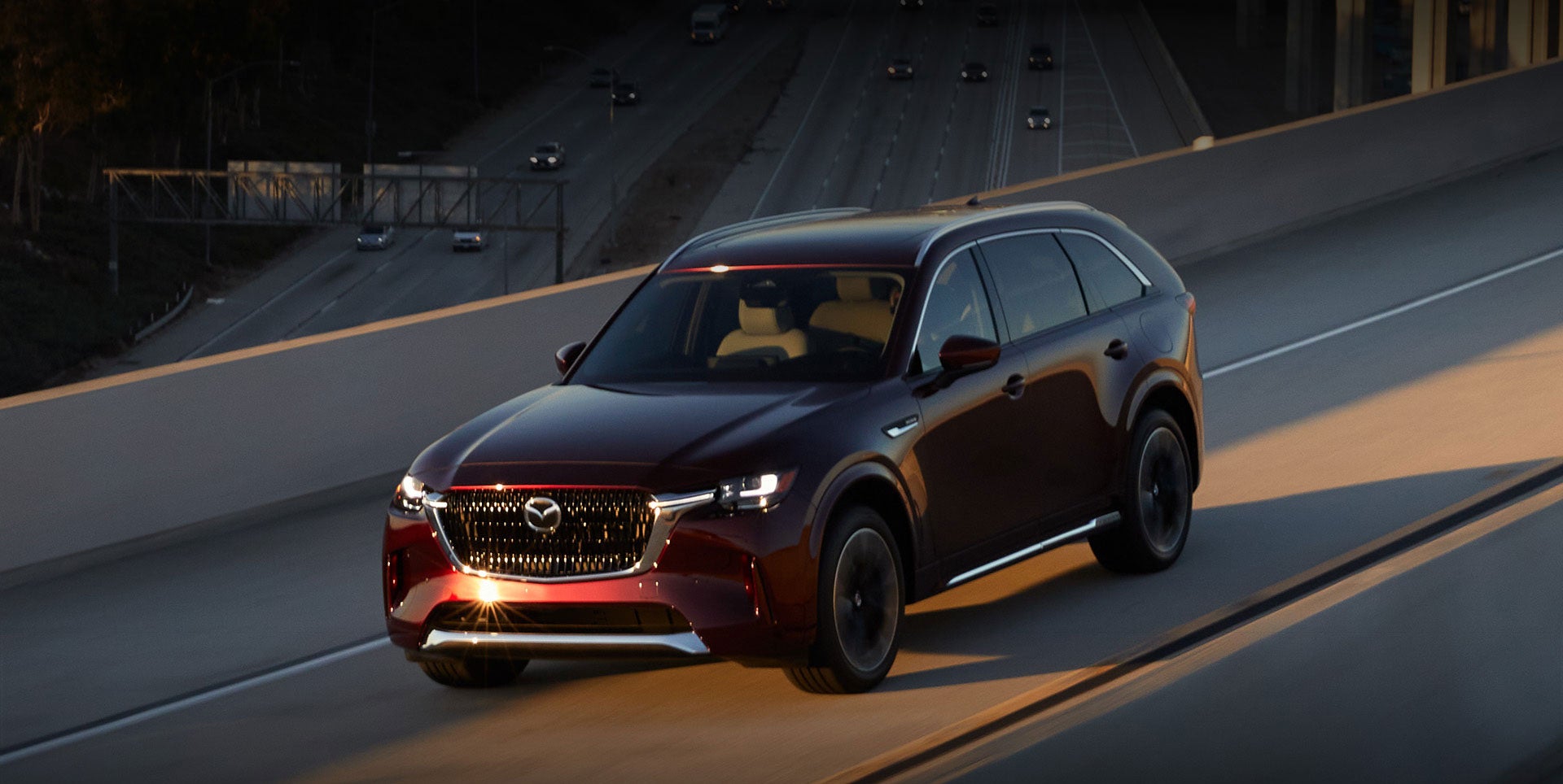 front left angle view of a glossy wine red 2024 mazda cx-90 driving through an overpass