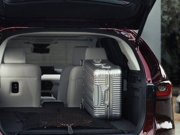 open hatchback of the 2024 mazda cx-90 cargo area with silver suitcase and view of backseats and front