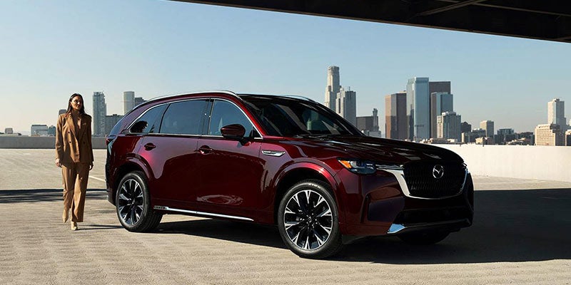 front right angle view of a glossy wine red 2024 mazda cx-90 parked with a city skyline in the background